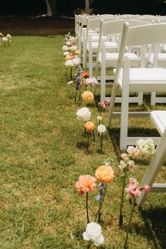 rows of white chairs with flowers on the grass