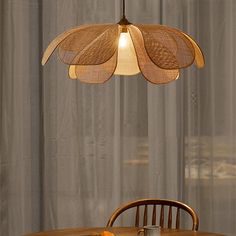 a wooden table and chair with a light hanging from it's center point, in front of a curtained window