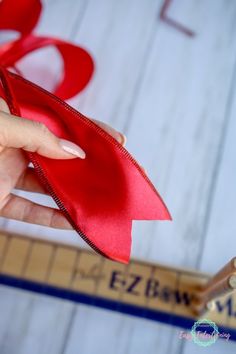 a person is holding a red ribbon in their hand and measuring it with a ruler