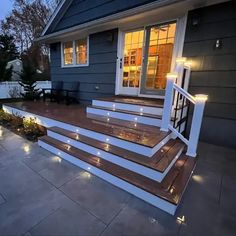 some lights are lit up on the steps in front of a house that is decorated with wood and white trim