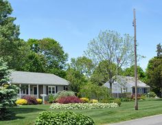 a house with lots of flowers in the front yard and trees on the other side