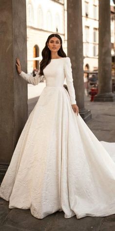 a woman in a white wedding dress standing next to pillars with her hands on her hips