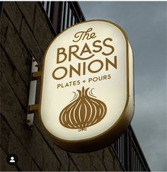 the brass onion sign is hanging from the side of a building with an overcast sky in the background