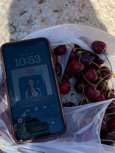 a cell phone sitting on top of a plastic bag filled with cherries next to a pile of grapes