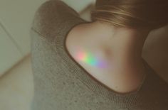 the back of a woman's neck with a rainbow colored light shining on it