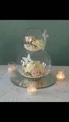 two tiered glass vases with flowers and candles on a tablecloth covered table