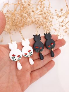 three black and white cat earrings with red flowers on them, sitting in someone's hand