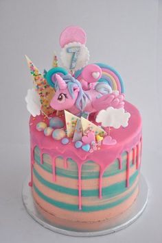 a birthday cake decorated with pink, blue and yellow icing has an unicorn on top