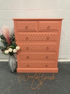 an orange dresser sitting next to a vase with flowers