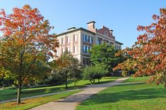 a large building sitting on the side of a lush green field next to trees with orange leaves