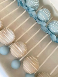 some blue and white cake pops are in a box with ribbons on them, along with other desserts