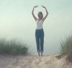 a woman standing on top of a sandy beach next to tall grass and sea oats