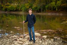 a young man holding a fishing pole while standing on rocks in front of a river