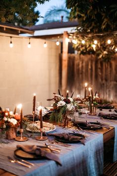 an outdoor dinner table set up with candles and place settings for the guests to enjoy