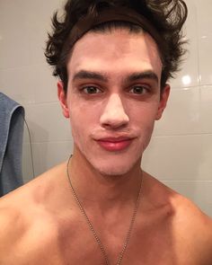 a young man with no shirt on taking a selfie in the bathroom while wearing a chain around his neck