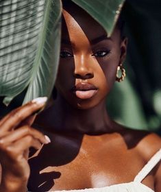 a woman in a white dress holding a large green leaf over her face and looking at the camera