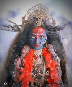 a woman with blue face paint and red flowers in her hair, wearing an elaborate headdress