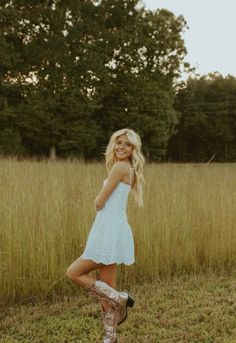 a beautiful blonde woman standing in a field with her legs crossed and wearing cowboy boots