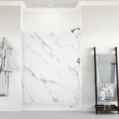 a bathroom with white walls and marble flooring is pictured in this image, there are towels hanging on the rack next to the shower door