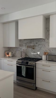 a kitchen with white cabinets and marble backsplash, stainless steel range hoods