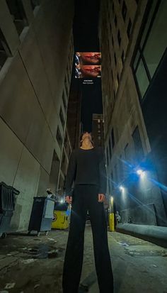 a woman standing in the middle of an alley way at night with her back turned to the camera