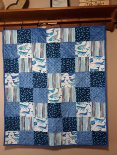 a blue and white quilt hanging on a wall next to a shelf with pictures above it