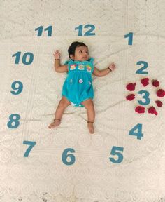 a baby laying on top of a white blanket next to a large clock with numbers