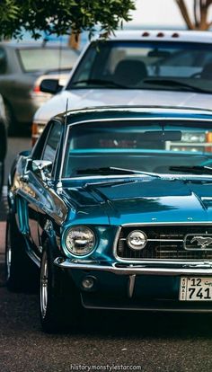 an old blue mustang parked on the side of the road with other cars behind it