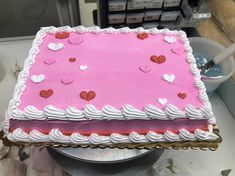 a pink cake with white icing and hearts on it sitting on top of a table