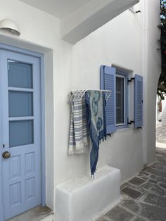 blue shutters and towels hanging on the outside wall of a white building with stone steps