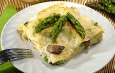 a white plate topped with lasagna covered in cheese and asparagus next to a fork