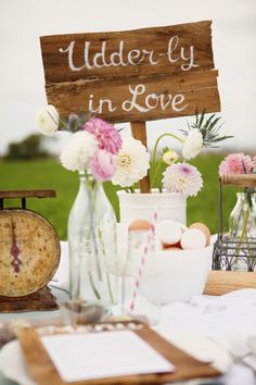 a table topped with vases filled with flowers next to a sign that says udderly in love