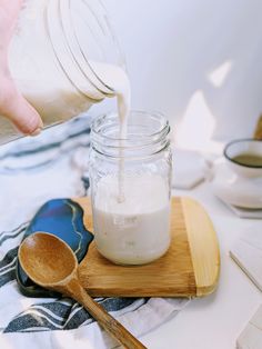 a person pouring milk into a jar on top of a cutting board with wooden spoons