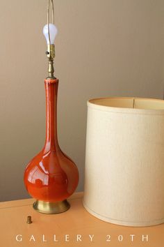 an orange vase sitting next to a lamp on top of a wooden table with a white lampshade