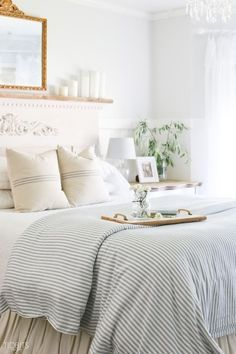 a bed with white sheets and pillows in a bedroom next to a chandelier