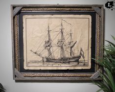 a drawing of a sailing ship is hanging on the wall next to a potted plant