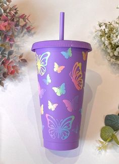 a purple cup with butterflies on it next to some flowers and leaves in the background