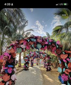 an archway decorated with colorful paper flowers and palm trees on the side of a road