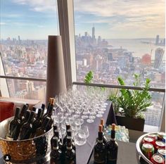 a table with wine glasses and bottles on it in front of a large window overlooking the city