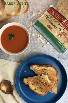 a blue plate topped with two pieces of toast next to a bowl of soup and bag of bread