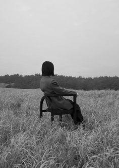 a person sitting on a chair in the middle of a field with tall grass and trees