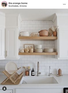 a kitchen with white cabinets and open shelving above the sink that is filled with dishes