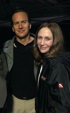 two people standing next to each other in front of a dark background with one person smiling at the camera