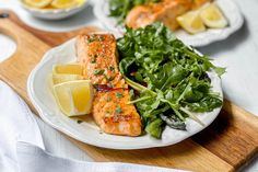 two plates with salmon, greens and lemons on them