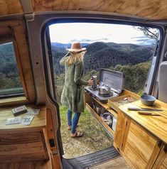 a woman standing in the back of a van looking out at mountains and trees from inside