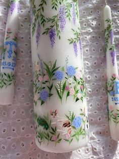 three vases with flowers painted on them sitting on a lace tablecloth next to each other