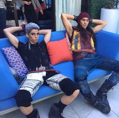 two people sitting on a blue couch with their arms behind their head and legs crossed