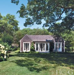 a small house in the middle of some trees and grass with white flowers around it