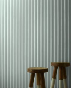 two wooden stools sitting next to each other in front of a white corrugated wall