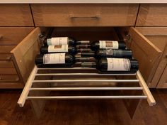 several bottles of wine are sitting on the bottom shelf of a pull out drawer in a kitchen